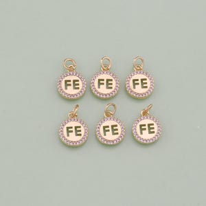 May include: Six gold-tone charms with a clear crystal encrusted border. Each charm features the letters "FE" in a cutout design.