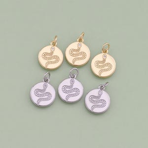 May include: Six gold and silver snake charm pendants with a clear rhinestone eye. The snake is coiled and the charms are round.