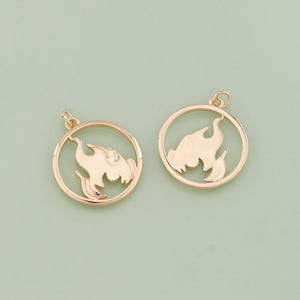 May include: Two gold-tone metal charms in the shape of a circle with a flame design cut out. The charms have a loop at the top for attaching to a necklace or bracelet.