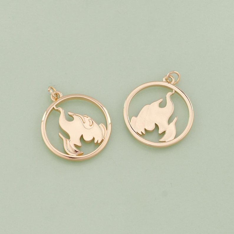 May include: Two gold-tone metal charms in the shape of a circle with a flame design cut out. The charms have a loop at the top for attaching to a necklace or bracelet.
