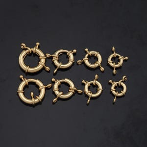 May include: Assortment of eight gold-toned metal lobster clasps of varying sizes. The clasps are round with a decorative design and have a spring-loaded mechanism.