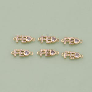 May include: Six gold-tone charms with the word "FE" and a clear heart-shaped rhinestone. Each charm has a loop on either side for attaching to a bracelet or necklace.