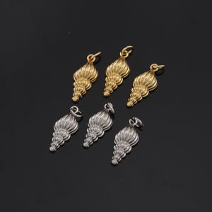 May include: Six gold and silver seashell charms with a detailed design. The charms have a loop at the top for attaching to jewelry.