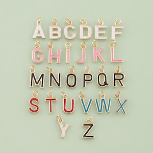 May include: A collection of gold-colored alphabet letter charms with colorful enamel detailing. Each letter is a different color, including white, pink, red, blue, and black. The charms are designed for jewelry making or crafting.