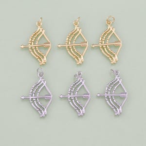 May include: Six gold and silver bow and arrow charms. The charms are detailed with a bow and arrow design and have a loop at the top for attaching to a necklace or bracelet.