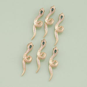 May include: Six gold snake charms with green gem eyes and clear crystal accents. The charms are arranged in a row on a light green background.