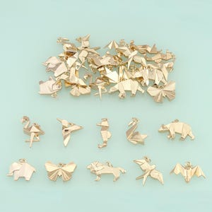 May include: Gold-colored origami charms in various animal shapes, including a flamingo, hummingbird, seahorse, swan, bear, elephant, butterfly, lion, bird, and bat. The charms are scattered on a light blue background.