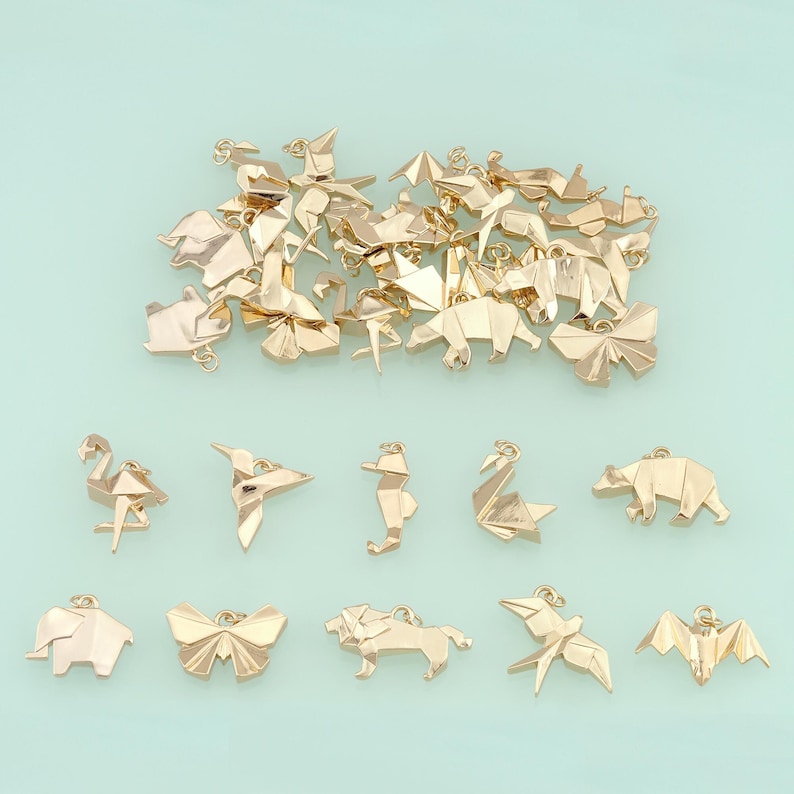 May include: Gold-colored origami charms in various animal shapes, including a flamingo, hummingbird, seahorse, swan, bear, elephant, butterfly, lion, bird, and bat. The charms are scattered on a light blue background.