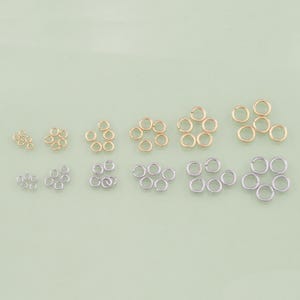 May include: Assortment of gold and silver jump rings in various sizes. The jump rings are arranged in rows by size.