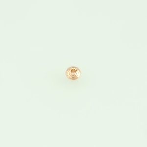 May include: A small, round, gold-colored bead with a detailed, etched pattern. The bead has a central hole and is likely used for jewelry making or crafting. The design features a series of small, repeating circular shapes.