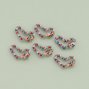 May include: Six colorful, geometric patterned, gold-toned metal lobster clasps. Each clasp is shaped like a heart and features a multi-colored enamel design.