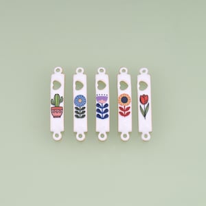 May include: Five white rectangular metal connector charms with rounded ends and small circular holes at the top and bottom. Each charm features a unique colorful floral or botanical graphic, including a cactus, blue flower, purple flower, sunflower, and red tulip.