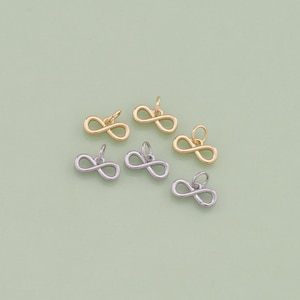 May include: Six infinity symbol charms, three silver and three gold, on a light green background.