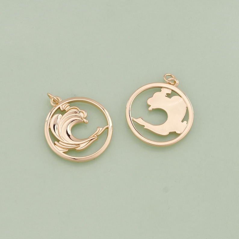 May include: Two gold-toned metal charms, one with a wave design and the other with a simple circle shape. Both charms have a loop for attaching to a necklace or bracelet.