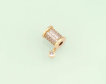 May include: Gold-toned charm with a cylinder shape covered in clear rhinestones and a dangling clear rhinestone.