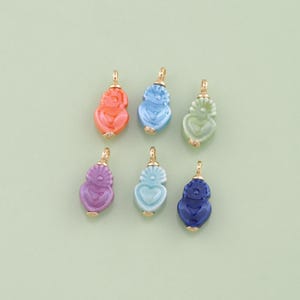 May include: A collection of six colorful pendant charms in shades of coral, blue, green, purple, light blue, and navy. Each charm features a heart-shaped design with a gold-colored bail for attaching to a chain or bracelet.