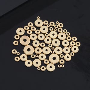 Könnte beinhalten: Eine große Gruppe von goldfarbenen Metall-Sprühringen in verschiedenen Größen. Die Sprühringe sind in einem lockeren Kreis auf einer schwarzen Oberfläche angeordnet.