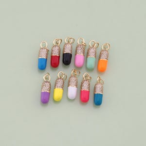 May include: Assortment of twelve colorful pill charm pendants. Each charm is gold-toned and features a clear crystal design. The charms are in various colors, including blue, red, pink, green, yellow, and orange.