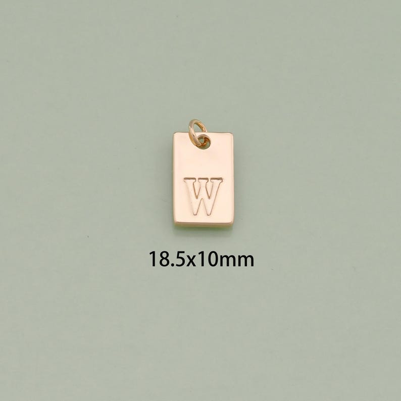 K&ouml;nnte beinhalten: Goldfarbener Metallanh&auml;nger mit dem Buchstaben "W" auf einem rechteckigen Anh&auml;nger graviert. Der Anh&auml;nger misst 18,5 x 10 mm.
