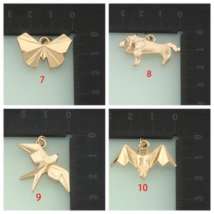 May include: Four gold-colored origami-style charms: a butterfly, a lion, a bird, and a bat. Each charm has a loop for attaching to jewelry. The charms are displayed against a black and white ruler background.