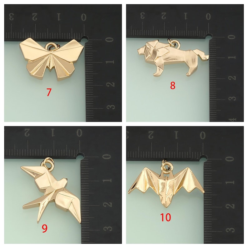 May include: Four gold-colored origami-style charms: a butterfly, a lion, a bird, and a bat. Each charm has a loop for attaching to jewelry. The charms are displayed against a black and white ruler background.