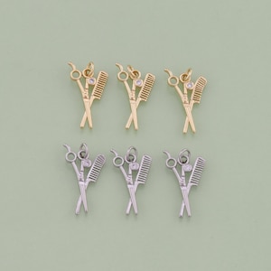 May include: Six gold and silver charms in the shape of crossed hairdressing scissors and combs. The charms have a single clear rhinestone in the center.