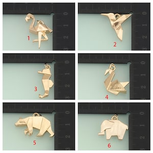 May include: A collection of six gold-colored origami-style pendants. The pendants depict a flamingo, hummingbird, seahorse, swan, bear, and elephant. Each pendant has a small loop for attaching to a chain or bracelet.