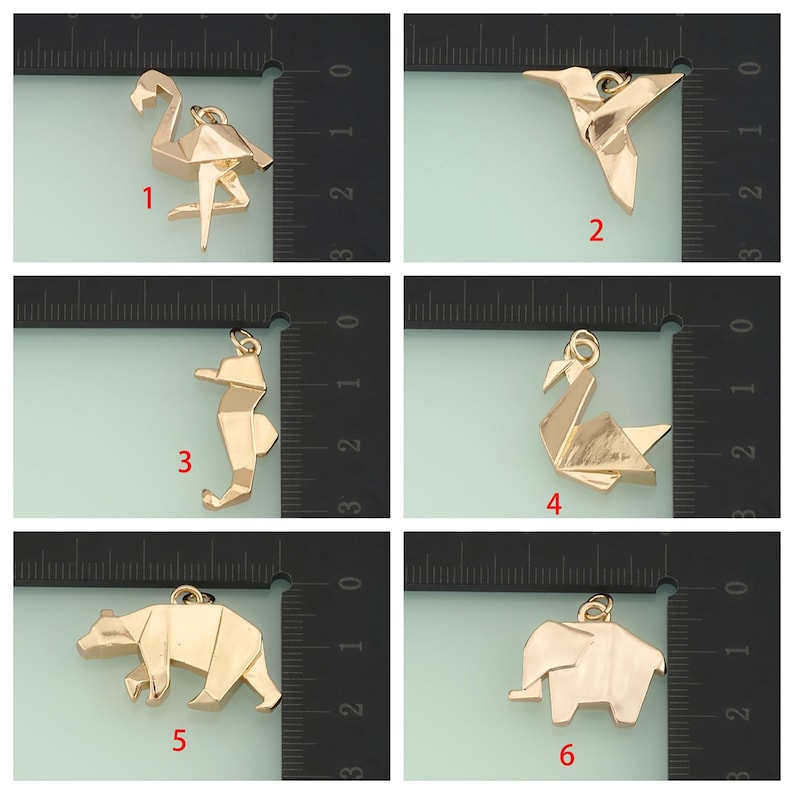 May include: A collection of six gold-colored origami-style pendants. The pendants depict a flamingo, hummingbird, seahorse, swan, bear, and elephant. Each pendant has a small loop for attaching to a chain or bracelet.