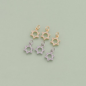 May include: Five gold and silver charms in the shape of a Star of David with clear rhinestones. The charms are on a light green background.