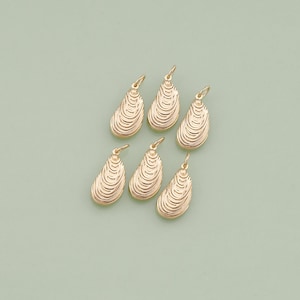 May include: Six gold-colored clam shell charms with a textured surface. The charms are perfect for jewelry making or adding a touch of coastal style to your crafts.