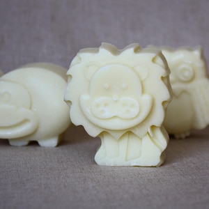 May include: Ivory-colored soap bars in the shapes of a lion, a hippo, and an owl. The lion soap has a detailed face and mane. The hippo is rounded, and the owl has detailed feather impressions. The soaps are arranged on a neutral-toned surface.
