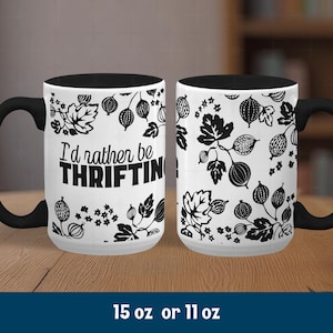 Puede incluir: Taza de cerámica blanca con asa e interior negros. La taza presenta un diseño botánico en blanco y negro con el texto "I'd rather be THRIFTING". La taza está disponible en 444 ml o 325 ml.