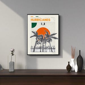 K&ouml;nnte beinhalten: Ein schwarzer gerahmter Poster mit wei&szlig;em Hintergrund und einer Grafik von Palmen und einer untergehenden Sonne. Der Text "University of Miami Hurricanes 1925" ist auf dem Poster gedruckt.
