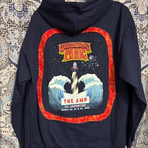 May include: A navy blue hoodie with a red and orange embroidered patch featuring a lighthouse, waves, and the text "WIDESPREAD PANIC", "LIVE AT THE AMP", "ST. AUGUSTINE", and "MARCH 25, 26 & 27, 2022".