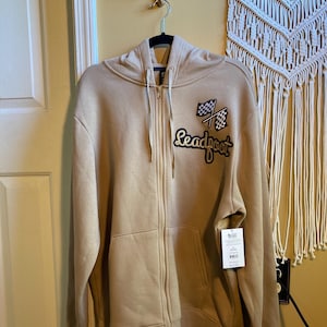 May include: A beige zip-up hoodie with a black and white checkered flag and the word "Leadfoot" in gold lettering on the front.