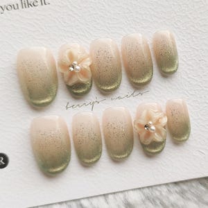 Könnte beinhalten: Ein Set künstlicher Nägel mit einem Farbverlauf von Nude zu Grün. Einige Nägel haben eine 3D-Blume mit Perlendetails. Die Karte trägt die Aufschrift "NAIL TIP DESIGN" und "Thank you for choosing my aesthetic. I hope you like it."