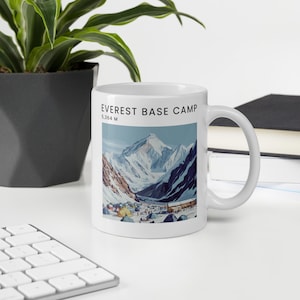 Puede incluir: Taza de cerámica blanca con una imagen colorida del Monte Everest y el campamento base. El texto "EVEREST BASE CAMP 5,364 M" está impreso en la taza.