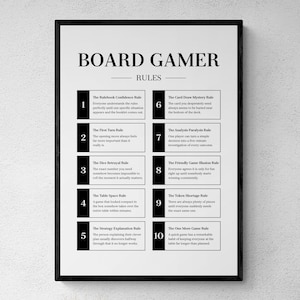 May include: A framed wall print featuring the text BOARD GAMER RULES at the top, followed by a numbered list of ten humorous rules for board games. The design uses black text and black rectangular accents on a white background in a simple layout.