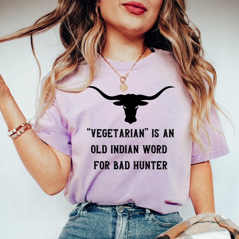 Puede incluir: Camiseta lila con un gr&aacute;fico negro de calavera de longhorn y el texto "Vegetarian is an old Indian word for bad hunter". La camiseta est&aacute; hecha de tela suave.