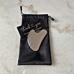 May include: A silver facial gua sha tool in a black velvet pouch with a thank you card that says "Thank you for supporting my business!"