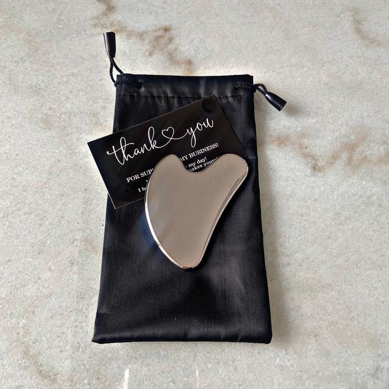 May include: A silver facial gua sha tool in a black velvet pouch with a thank you card that says "Thank you for supporting my business!"