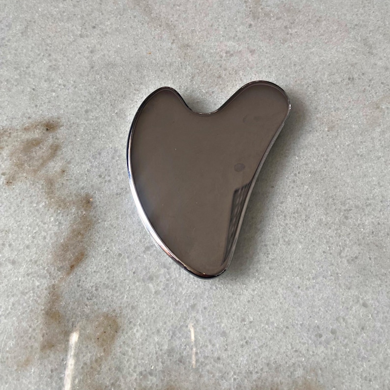 May include: A silver heart-shaped facial gua sha tool. This tool is used for massage and to promote lymphatic drainage.