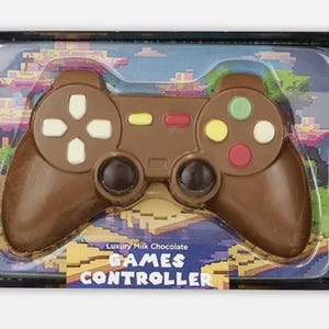 Può includere: Un controller per videogiochi di cioccolato al latte in una confezione di plastica trasparente. Il controller ha pulsanti bianchi, gialli, rossi e verdi. La confezione riporta le scritte "Luxury Milk Chocolate" e "GAMES CONTROLLER".