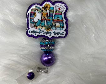 May include: Purple and turquoise glitter badge reel with a white background featuring the text "CNA Certified Nursing Assistant" with a red cross and a sunflower. The reel has a purple and turquoise crystal bead and a purple bead.