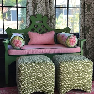 May include: A green wooden bench with a pink cushion and two matching green and white patterned ottomans. The bench has a lattice design on the back and floral patterned pillows.
