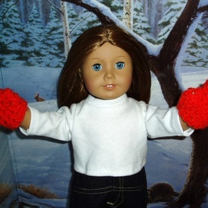 K&ouml;nnte beinhalten: Eine Puppe tr&auml;gt ein wei&szlig;es Langarmshirt und rote H&auml;kelhandschuhe. Die Puppe hat langes braunes Haar und blaue Augen. Die Puppe steht vor einem verschneiten Hintergrund.