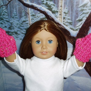 K&ouml;nnte beinhalten: Eine Puppe tr&auml;gt ein wei&szlig;es Langarmhemd und rosa geh&auml;kelte F&auml;ustlinge. Die Puppe hat langes braunes Haar und blaue Augen.