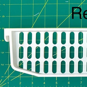 May include: White plastic replacement part for a kitchen appliance. The part has a grid of oval holes and is about 22 inches long.