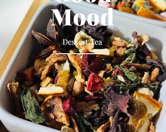 May include: A white ceramic bowl filled with a blend of dried fruit, herbs, and spices for a dessert tea. The tea blend includes orange peel, hibiscus flowers, star anise, and mint leaves. The bowl is on a wooden tray with the text "Good Mood Dessert Tea" and "VICOTEA" printed on it.
