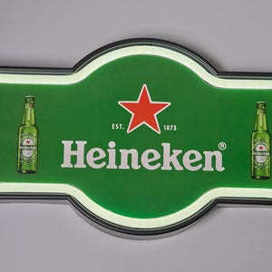 May include: A rectangular Heineken LED sign with rounded edges, featuring a green background, a red star, and the text "EST. 1873" and "Heineken". Two green beer bottles are printed on the left and right sides of the illuminated display.